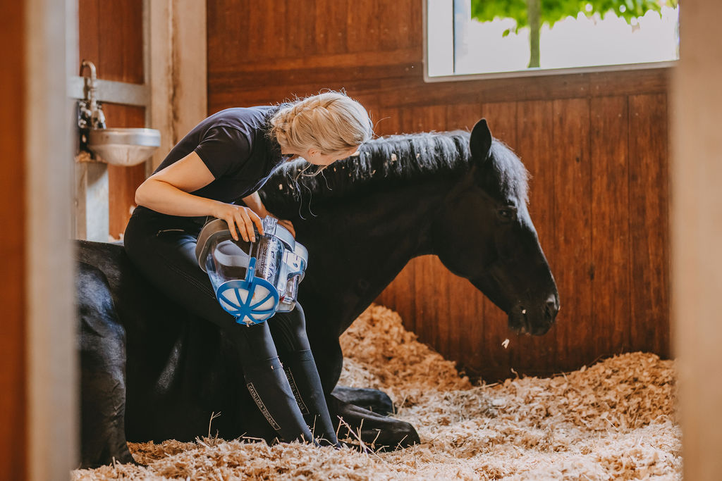 Frau sitzt bei liegendem Pferd im Stall und hält SaHoMa-II Inhalationsmaske in der Hand